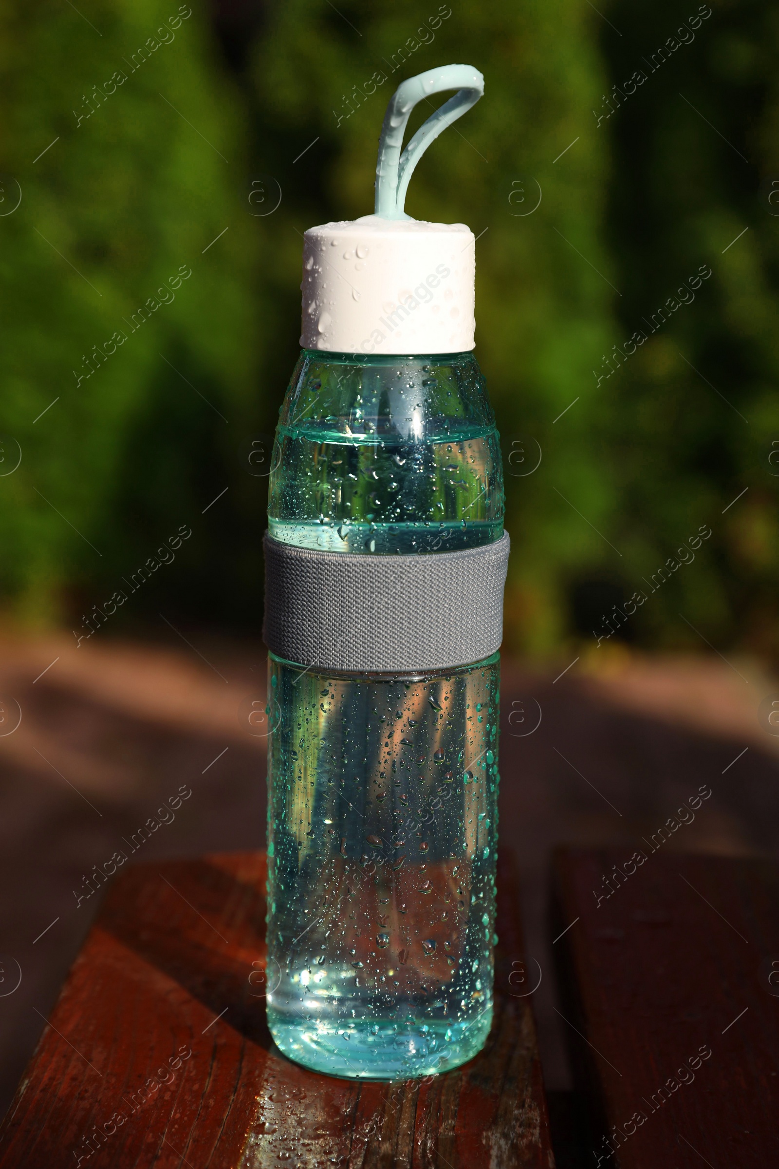 Photo of Glass bottle of fresh water on wooden table outdoors