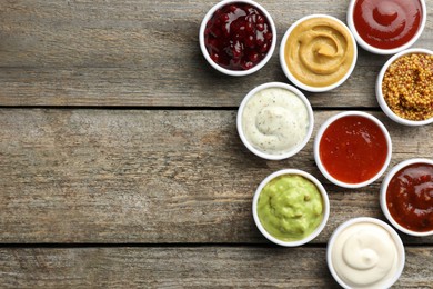 Photo of Different tasty sauces in bowls on wooden table, flat lay. Space for text