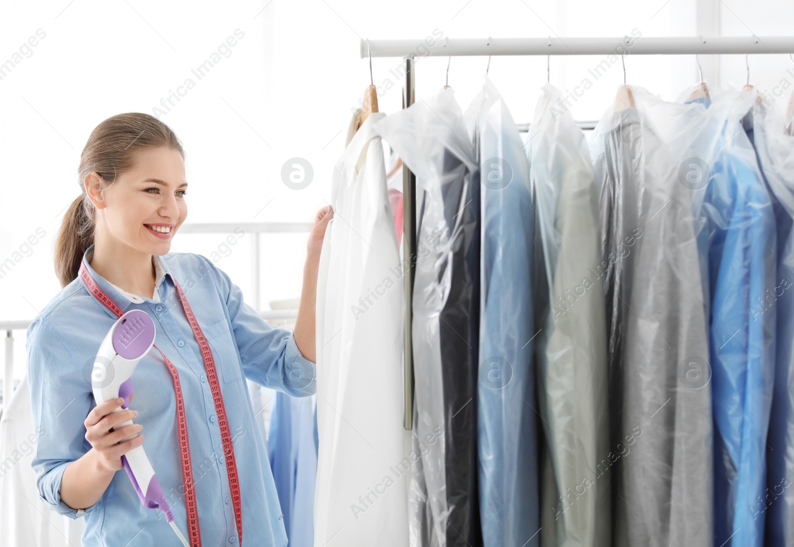 Photo of Young woman steaming shirt at dry-cleaner's