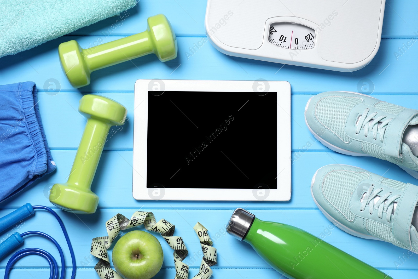 Photo of Tablet, sneakers and sports equipment on light blue wooden table, flat lay. Personal training