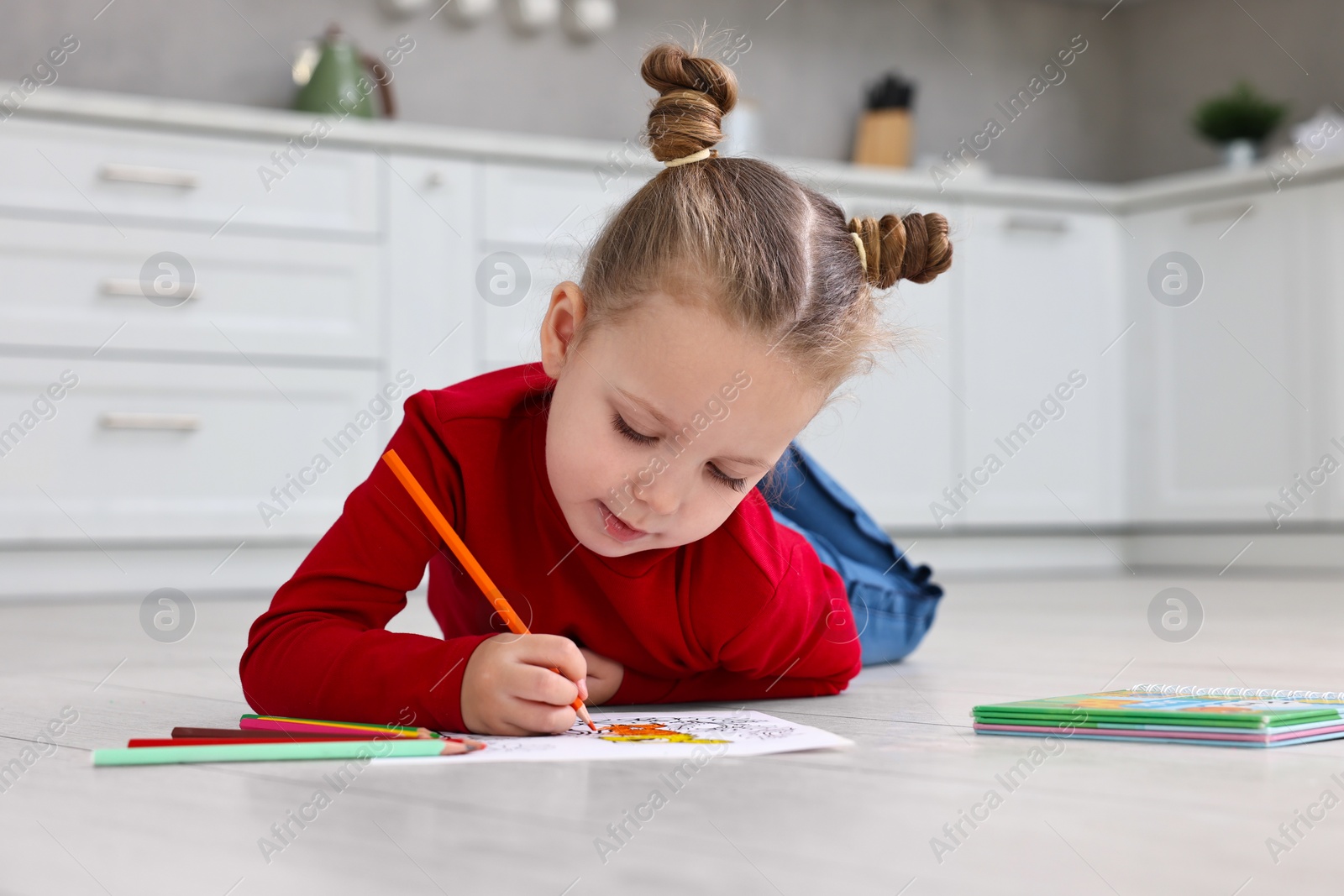 Photo of Cute little girl coloring on warm floor in kitchen. Heating system