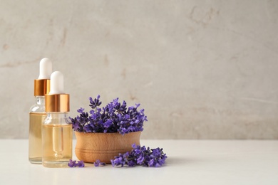 Bottles of essential oil and lavender flowers on white wooden table. Space for text