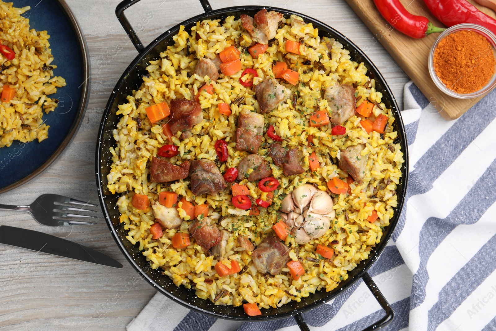 Photo of Delicious pilaf with meat, carrot and chili pepper served on wooden table, flat lay