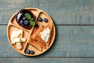 Photo of Tasty toasts with butter and blueberries on light blue wooden table, top view. Space for text