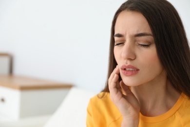 Young woman suffering from strong tooth pain at home, space for text