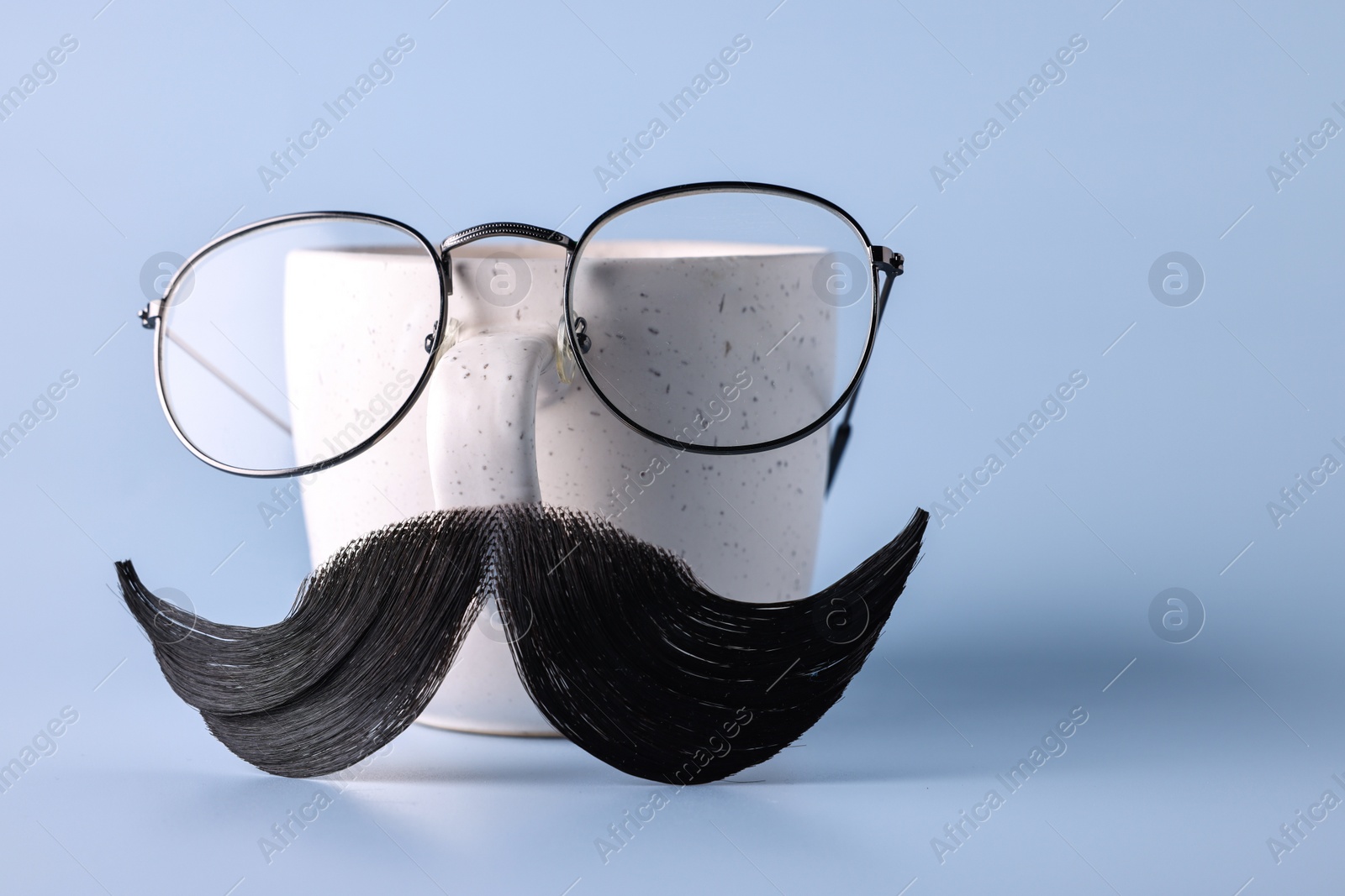 Photo of Man's face made of artificial mustache, glasses and cup on light blue background. Space for text