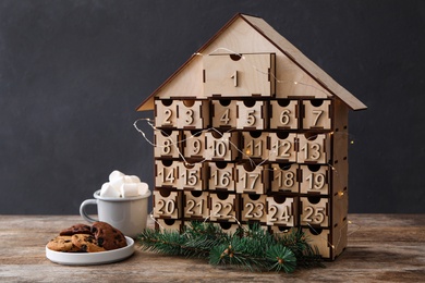 House shaped Christmas advent calendar, cookies and hot cocoa drink on wooden table
