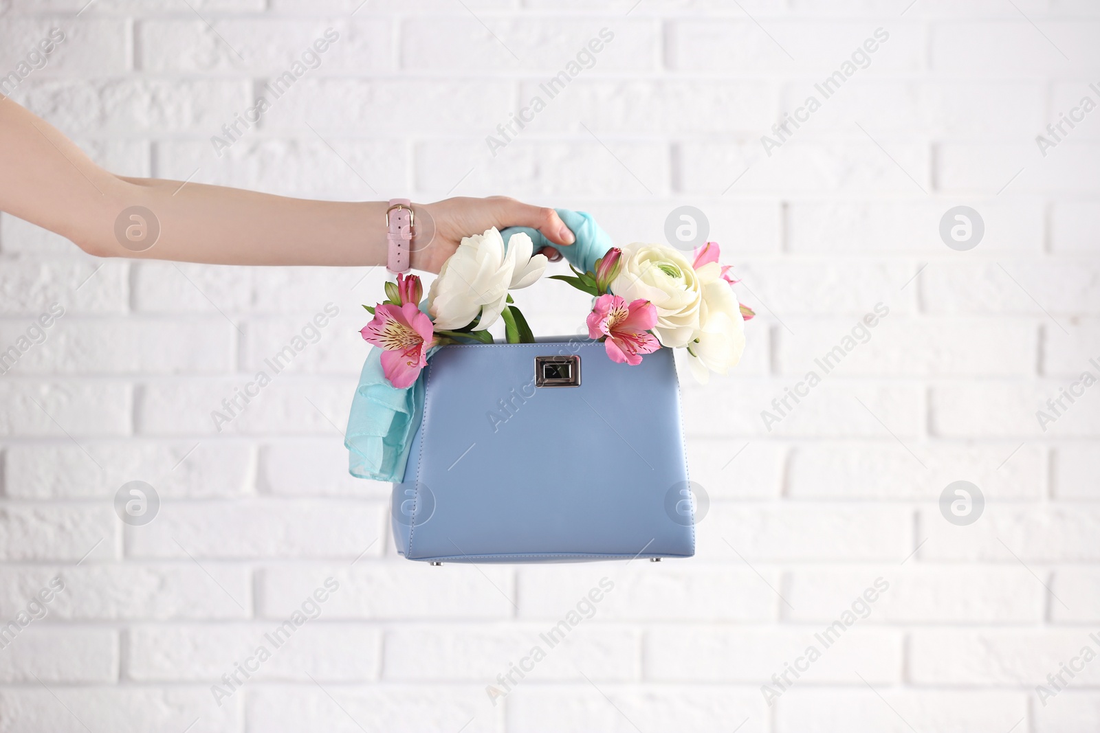 Photo of Woman holding elegant handbag with spring flowers against white brick wall, closeup