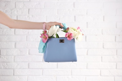 Photo of Woman holding elegant handbag with spring flowers against white brick wall, closeup