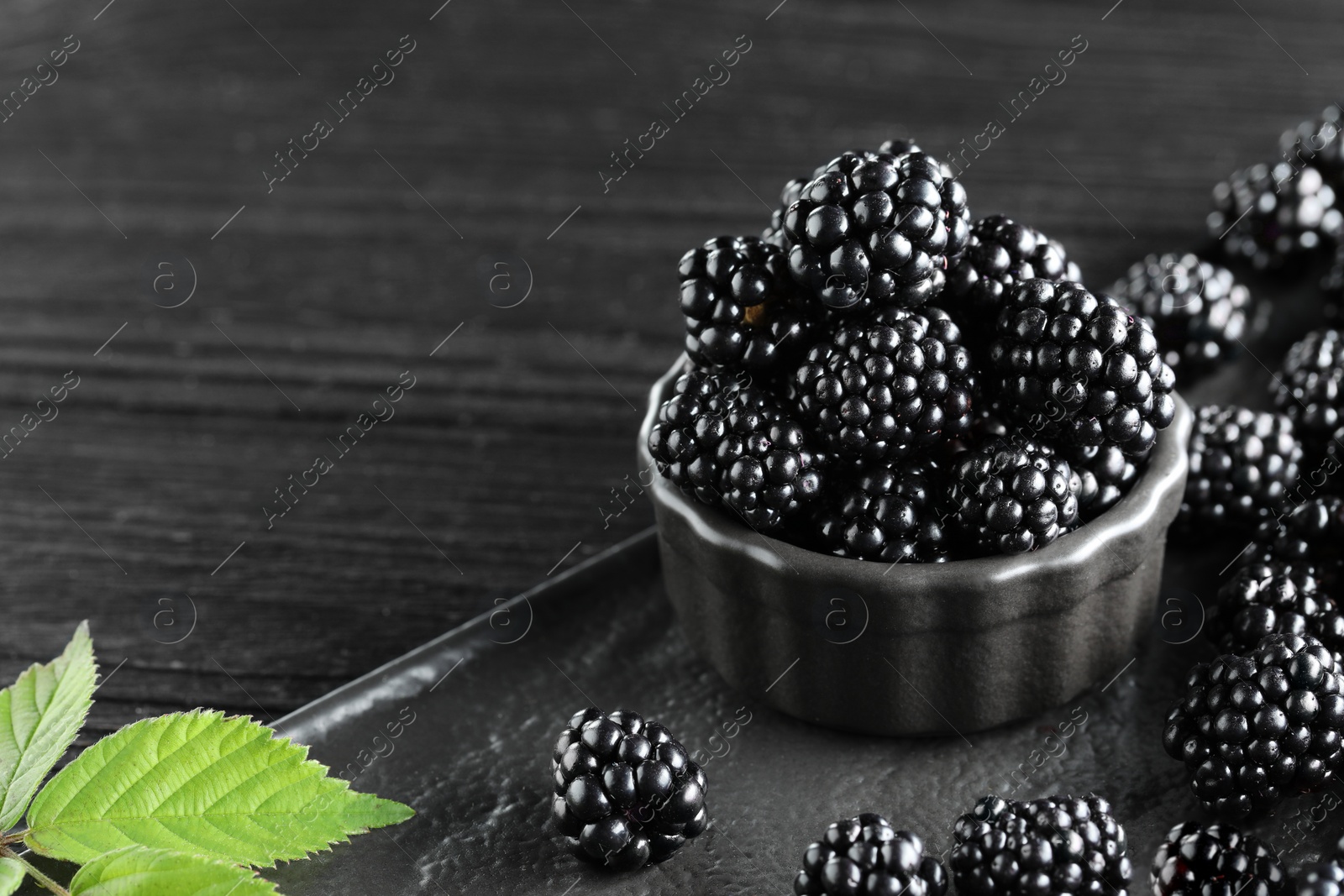 Photo of Fresh ripe blackberries and leaves on black wooden table. Space for text