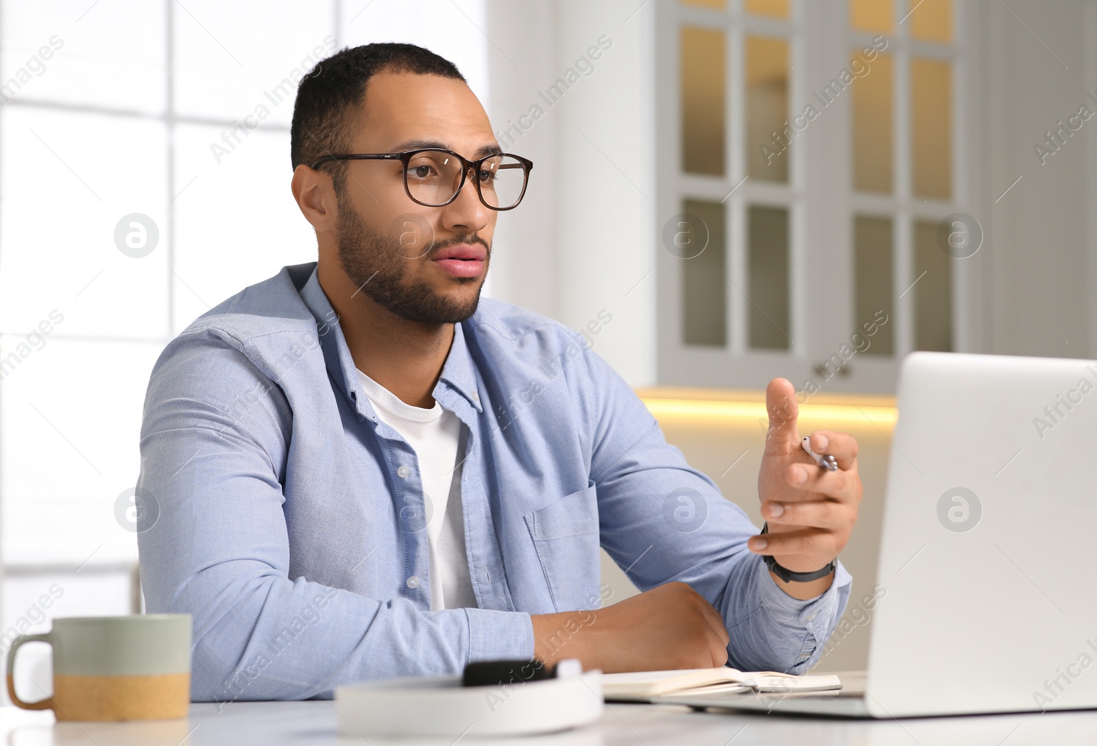 Photo of Young man having online video chat at desk in kitchen. Home office