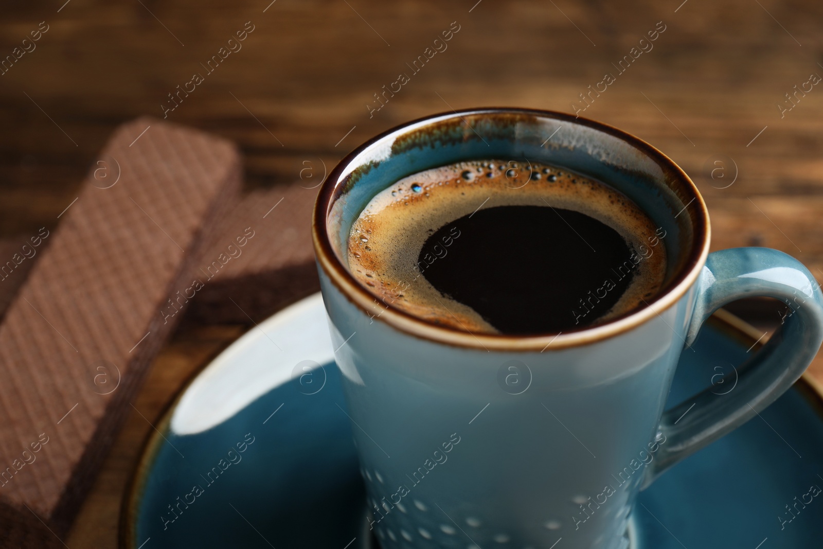 Photo of Delicious coffee and wafers for breakfast on wooden table, closeup