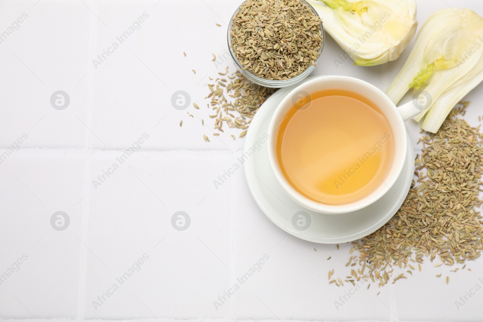 Photo of Fennel tea in cup, seeds and fresh vegetable on white tiled table, flat lay. Space for text