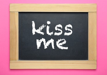 Small chalkboard with phrase Kiss Me on pink background, top view