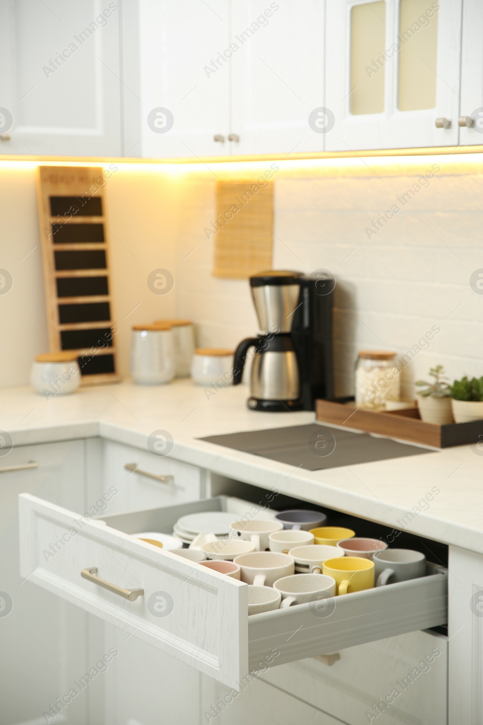 Photo of Open drawer with cups and coffeemaker on countertop in kitchen