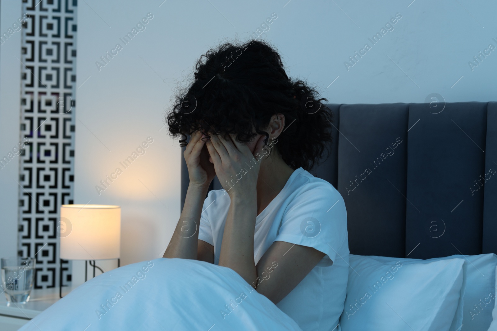 Photo of Young woman suffering from headache in bed at night