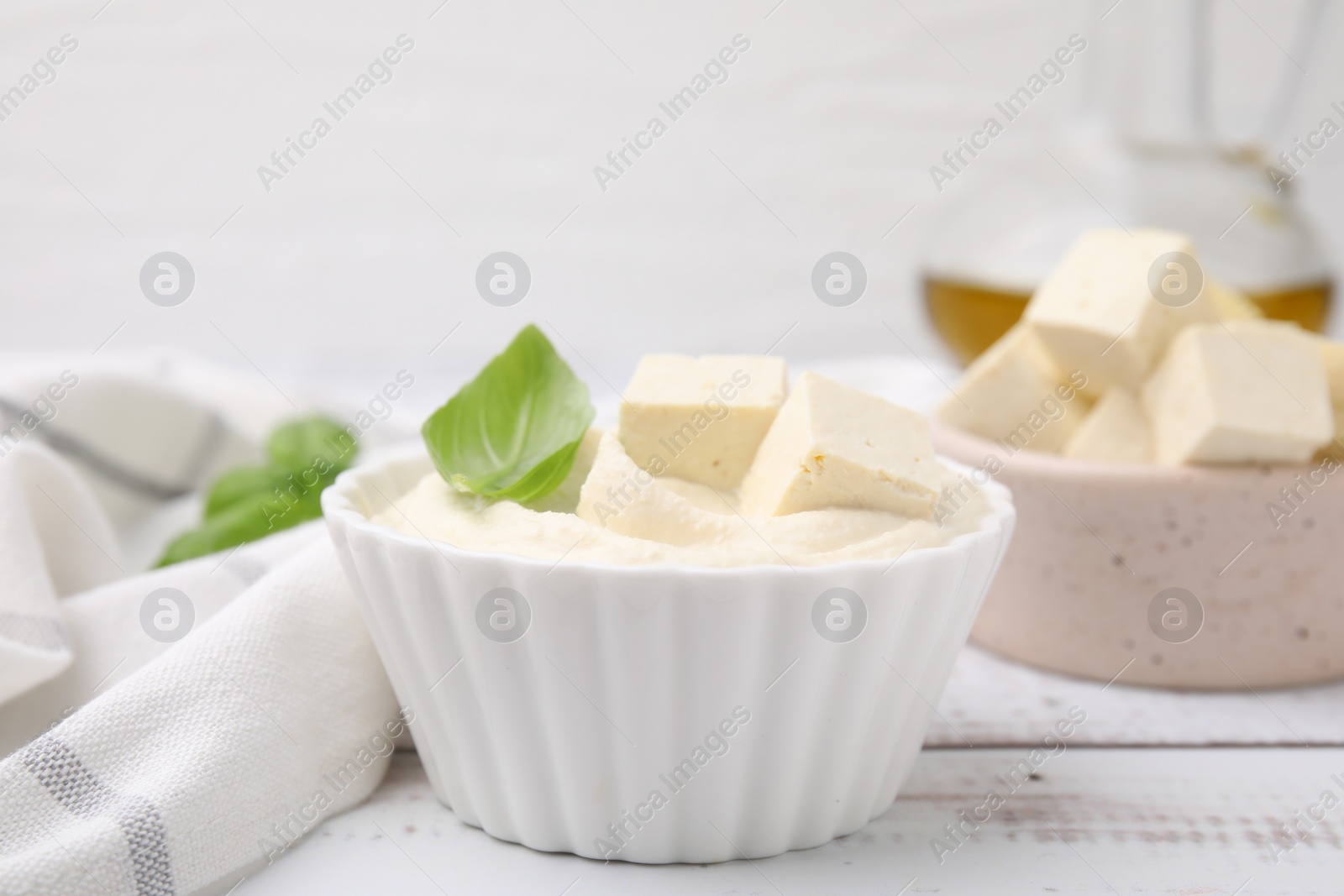 Photo of Delicious tofu sauce and basil leaves on white wooden table, closeup