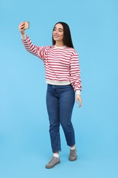 Photo of Smiling young woman taking selfie with smartphone on light blue background