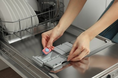 Photo of Woman putting detergent tablet into open dishwasher, closeup