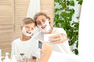 Father and son taking selfie with shaving foam on faces in bathroom