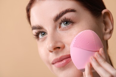 Photo of Washing face. Young woman with cleansing brush on beige background, closeup