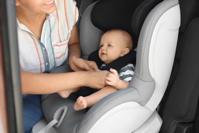 Photo of Mother fastening baby to child safety seat inside of car