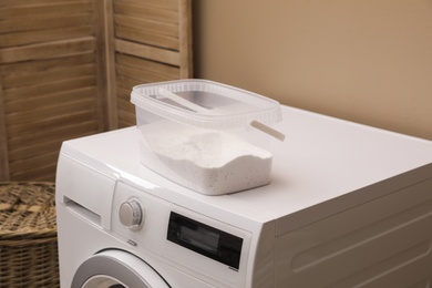 Plastic container with detergent powder on washing machine in laundry room