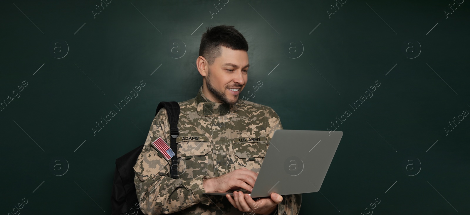 Image of Military education. Cadet with backpack and laptop near green chalkboard