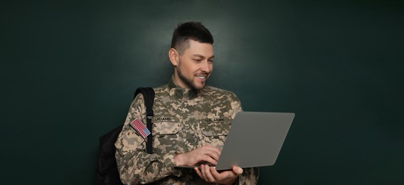 Military education. Cadet with backpack and laptop near green chalkboard