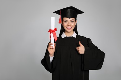 Photo of Happy student with graduation hat and diploma on grey background. Space for text