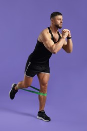 Photo of Muscular man exercising with elastic resistance band on purple background