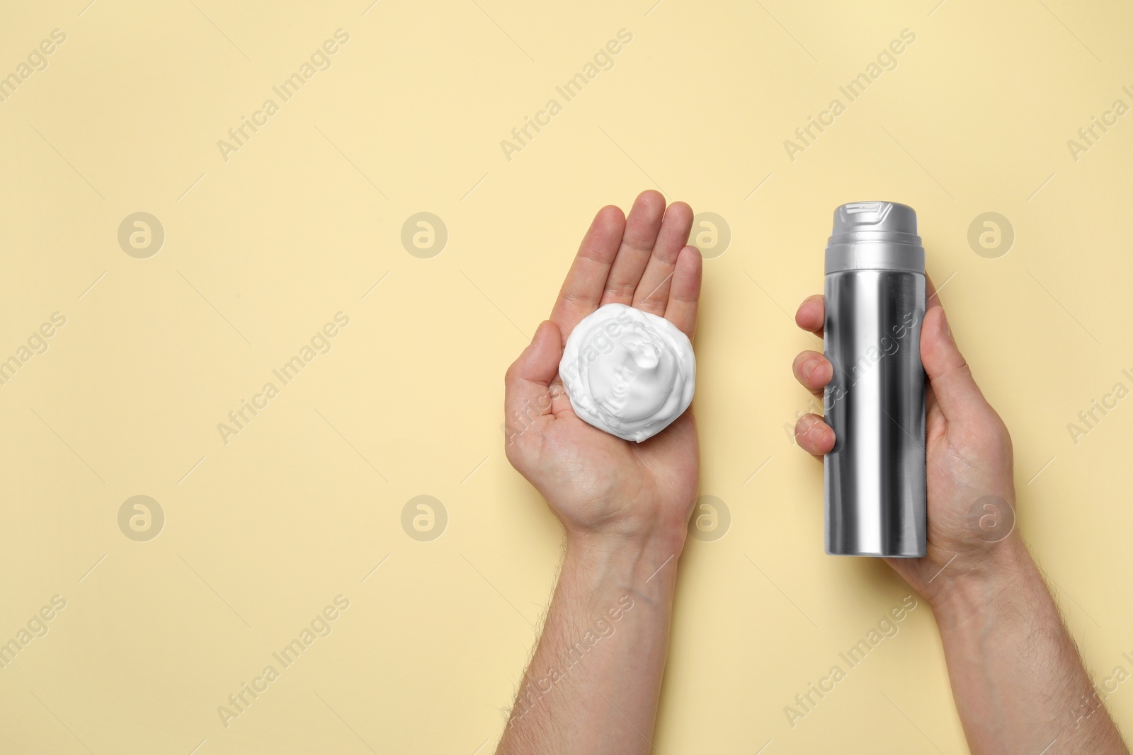 Photo of Man holding shaving foam and bottle on beige background, top view. Space for text