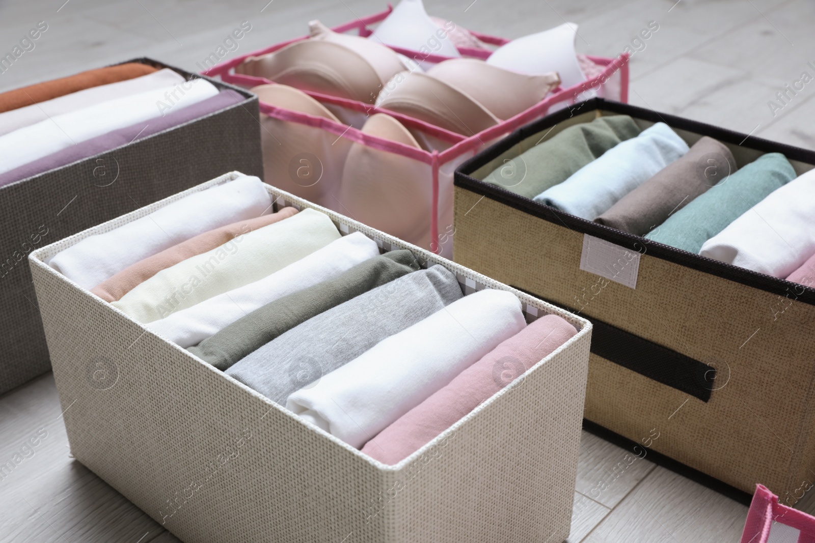 Photo of Different cases and organizer with folded clothes on white wooden background, closeup. Vertical storage