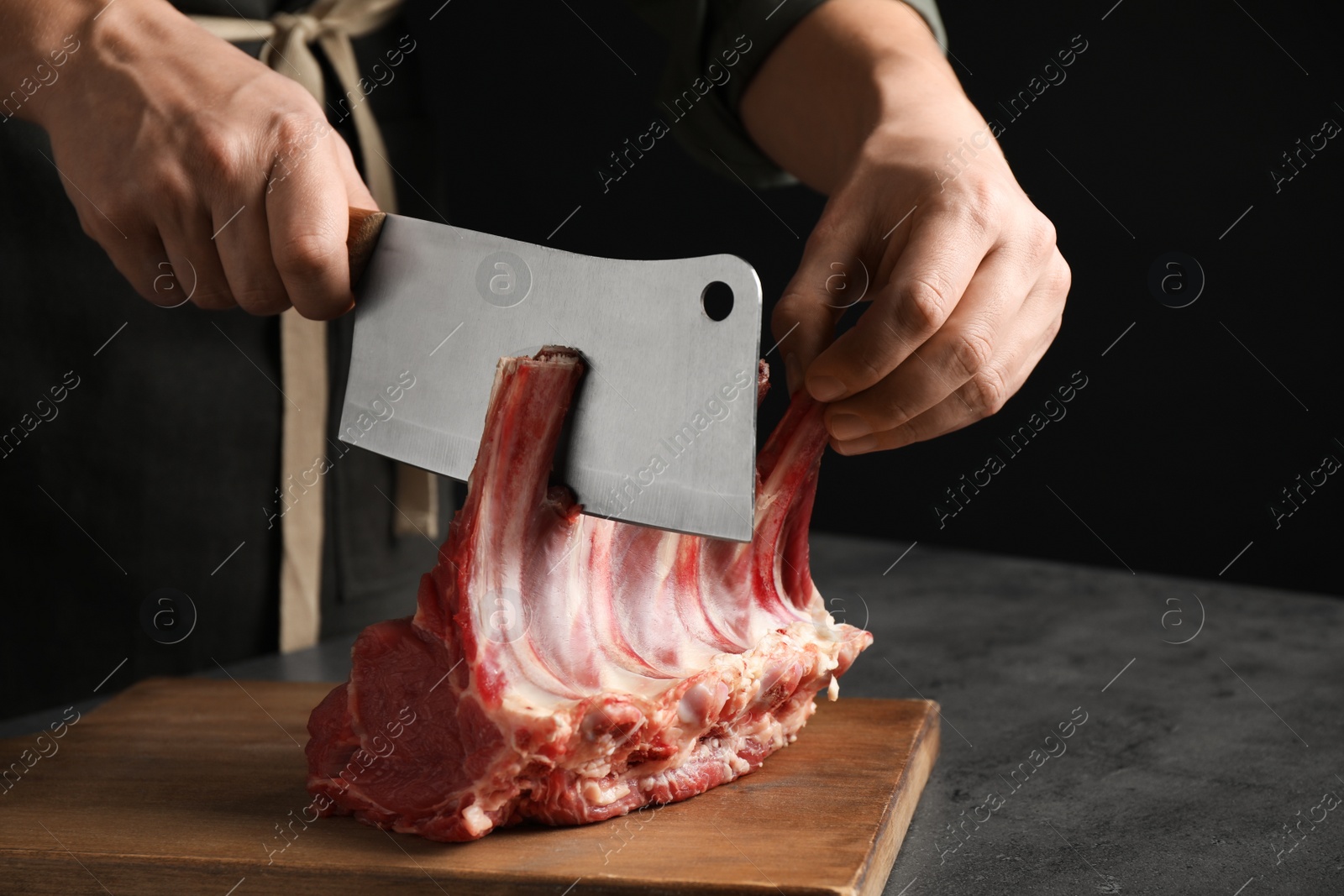 Photo of Man cutting raw ribs at grey table, closeup