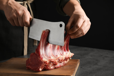 Photo of Man cutting raw ribs at grey table, closeup