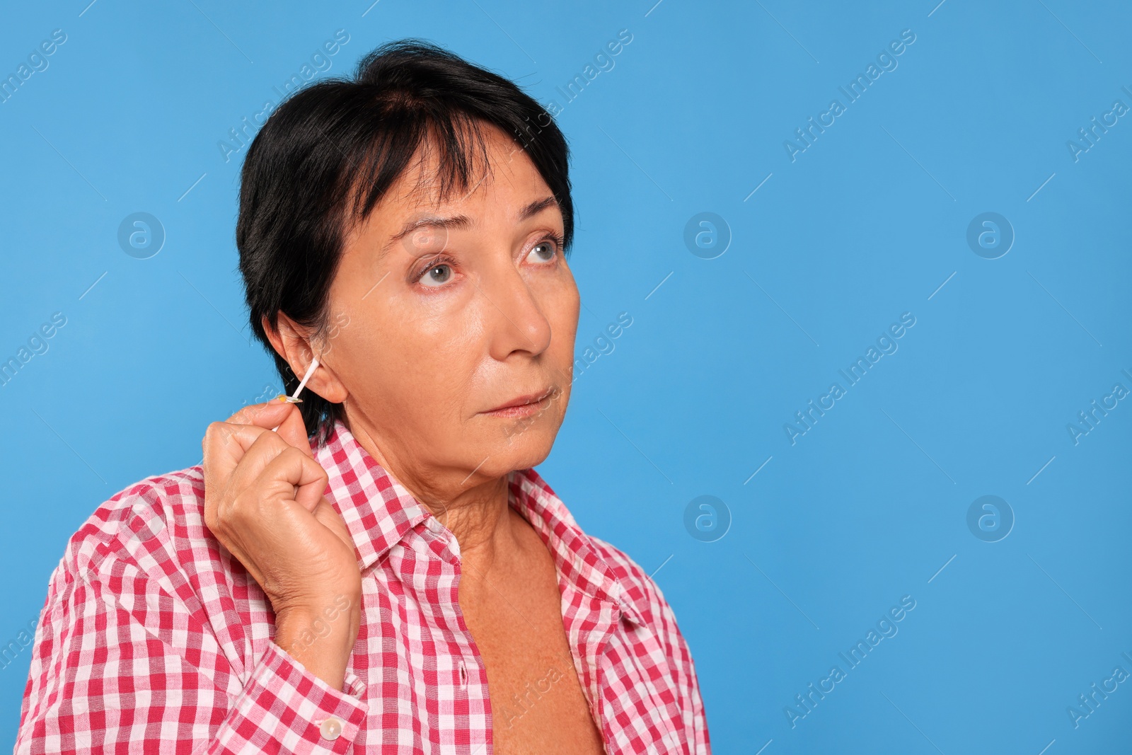 Photo of Senior woman cleaning ear with cotton swab on light blue background. Space for text