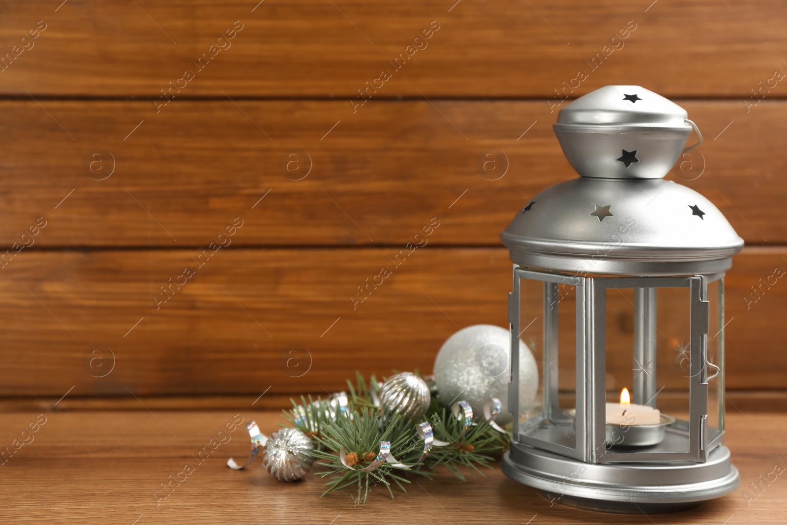 Photo of Christmas lantern with burning candle and festive decor on wooden table. Space for text