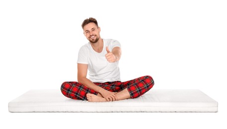 Photo of Smiling man sitting on soft mattress and showing thumb up against white background