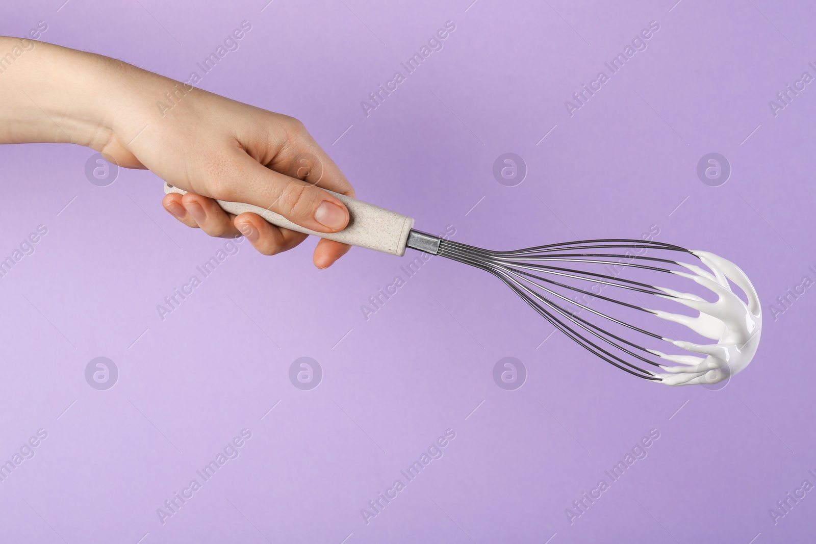 Photo of Woman holding whisk with whipped cream on violet background, closeup