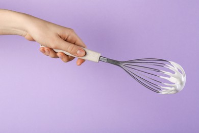 Photo of Woman holding whisk with whipped cream on violet background, closeup