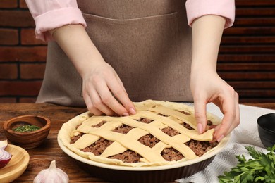 Woman making lattice top for meat pie at wooden table, closeup