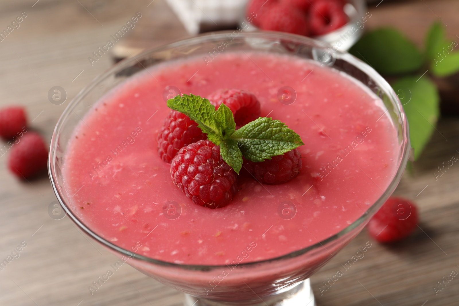 Photo of Delicious raspberry mousse with mint in glass dish, closeup