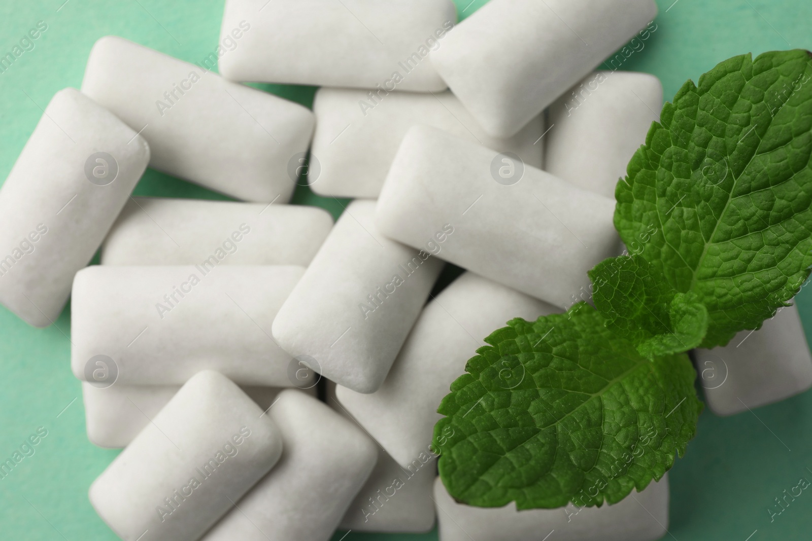 Photo of Tasty white chewing gums and mint leaves on turquoise background, top view