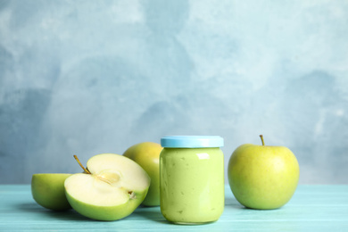 Jar with baby food and fresh apples on wooden table against light blue background, space for text