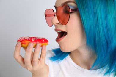 Photo of Young woman with bright dyed hair holding donut on light grey background, closeup