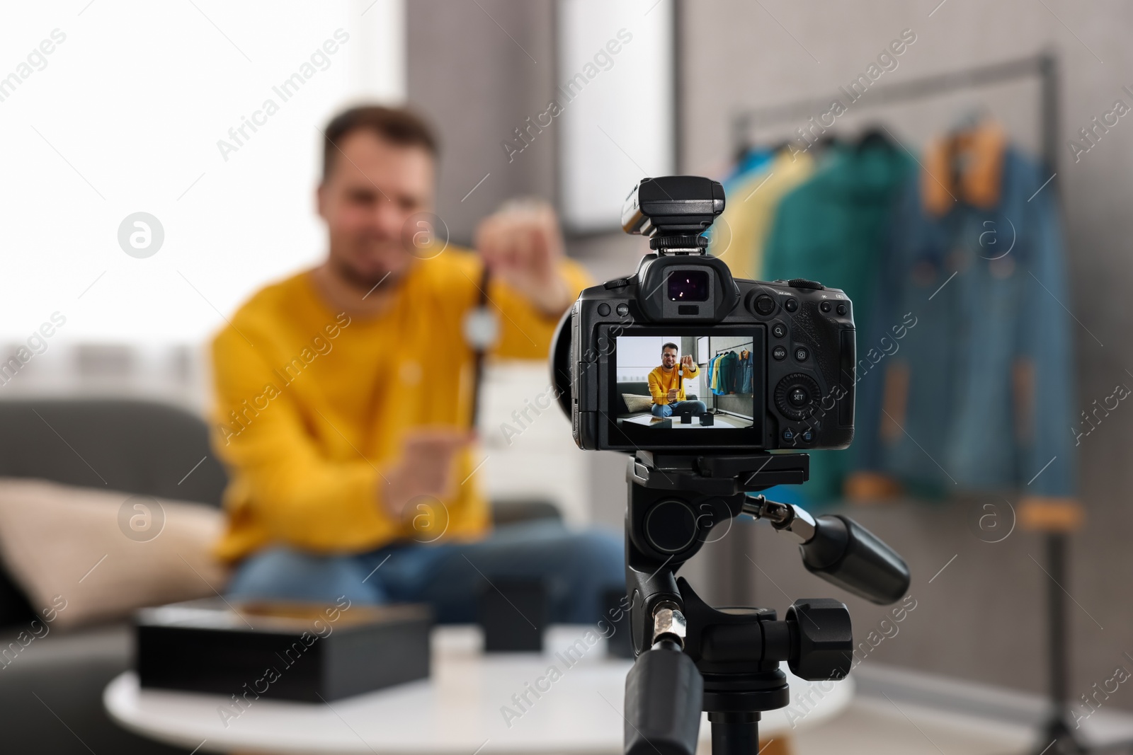 Photo of Fashion blogger showing wristwatch while recording video at home, focus on camera