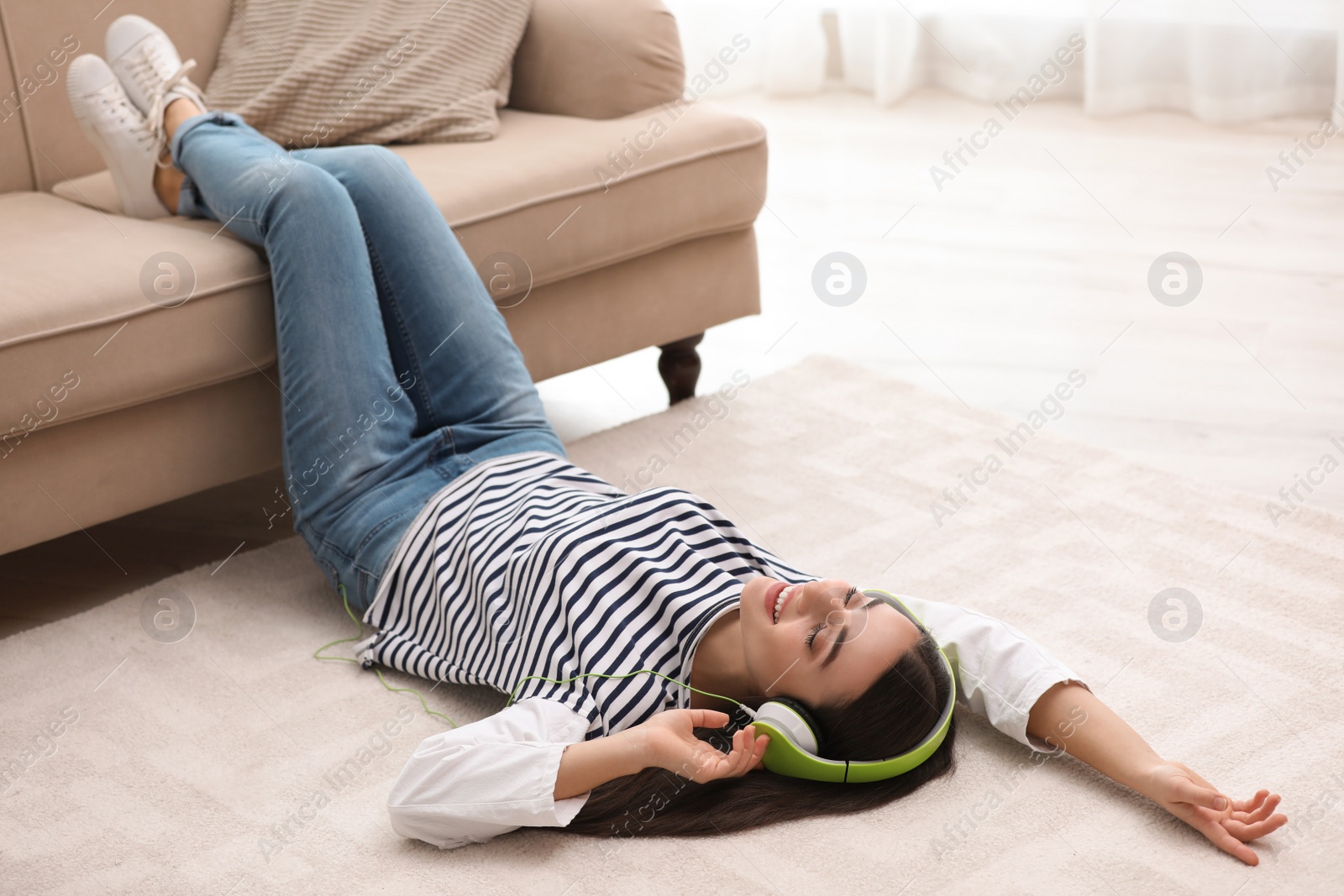 Photo of Young woman with headphones listening to music on floor in living room