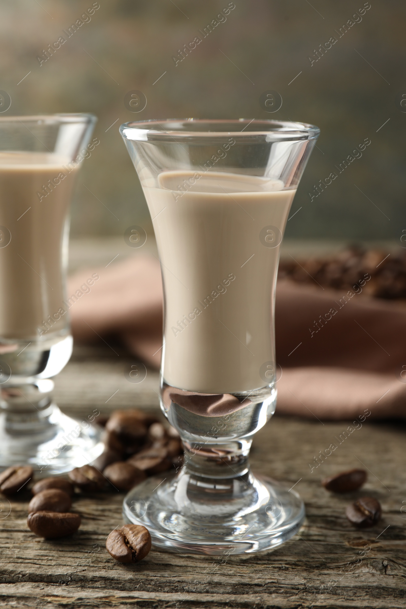 Photo of Coffee cream liqueur in glasses and beans on wooden table, closeup