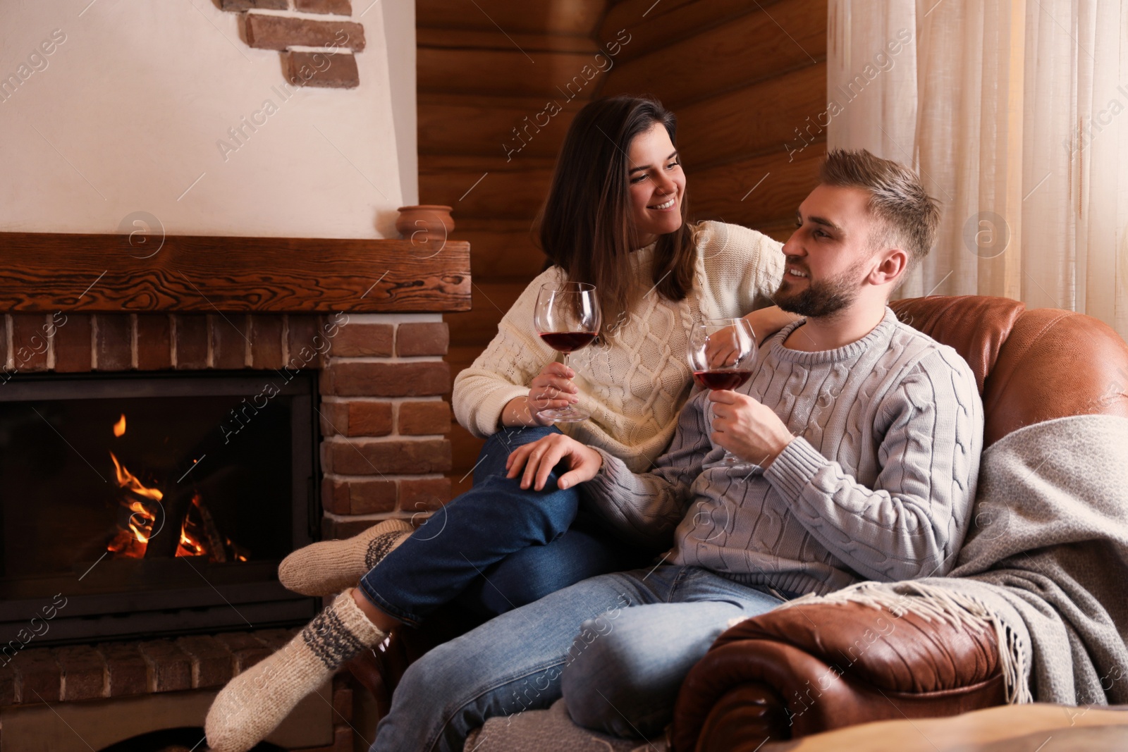 Photo of Lovely couple with glasses of wine resting near fireplace at home. Winter vacation