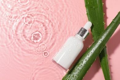 Photo of Bottle of cosmetic product and aloe leaves in water on pink background, flat lay. Space for text